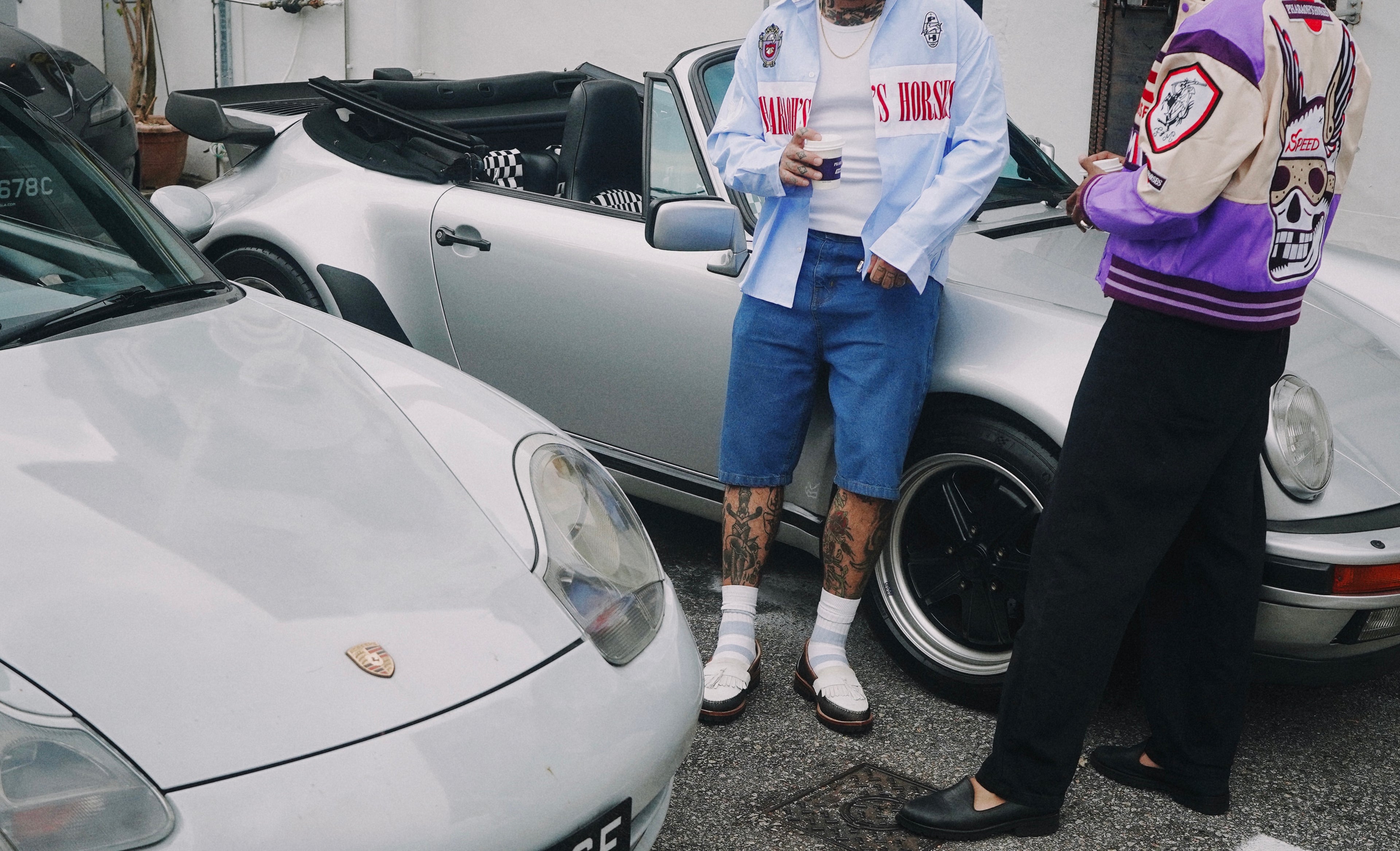 Two people standing next to a white Porsche car in a garage.